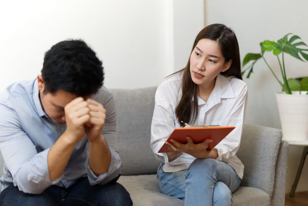 A Singaporean therapist seated across from a client on a couch, engaged in a therapy session.
