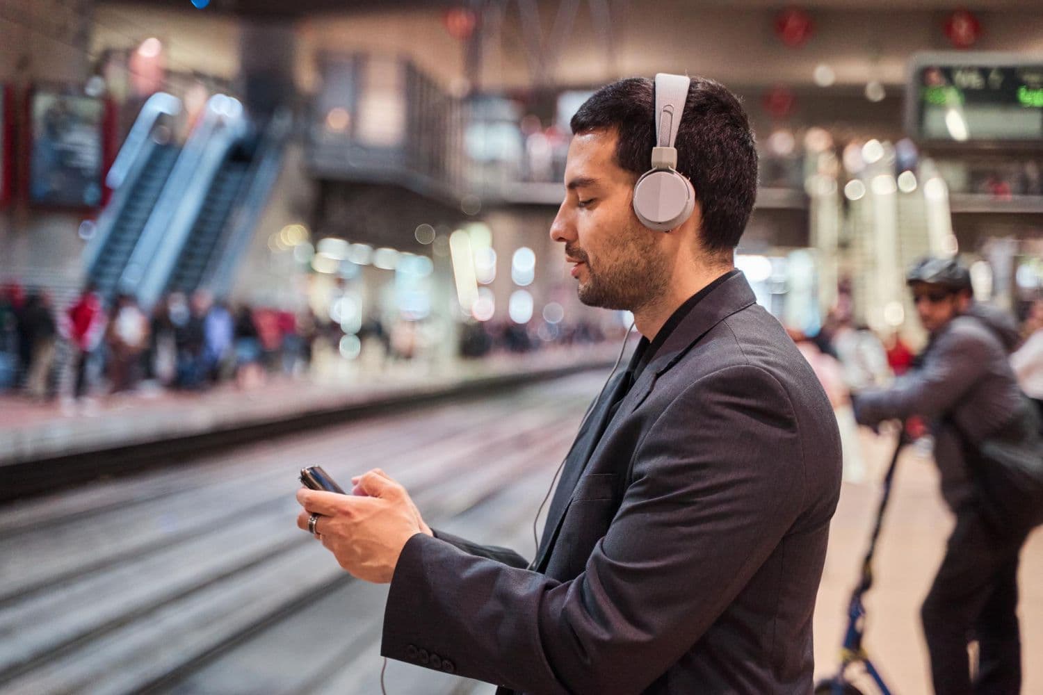 A man wearing headphones and standing with closed eyes at a train station. Counselling for social anxiety in Australia can help you learn coping tools such as this.