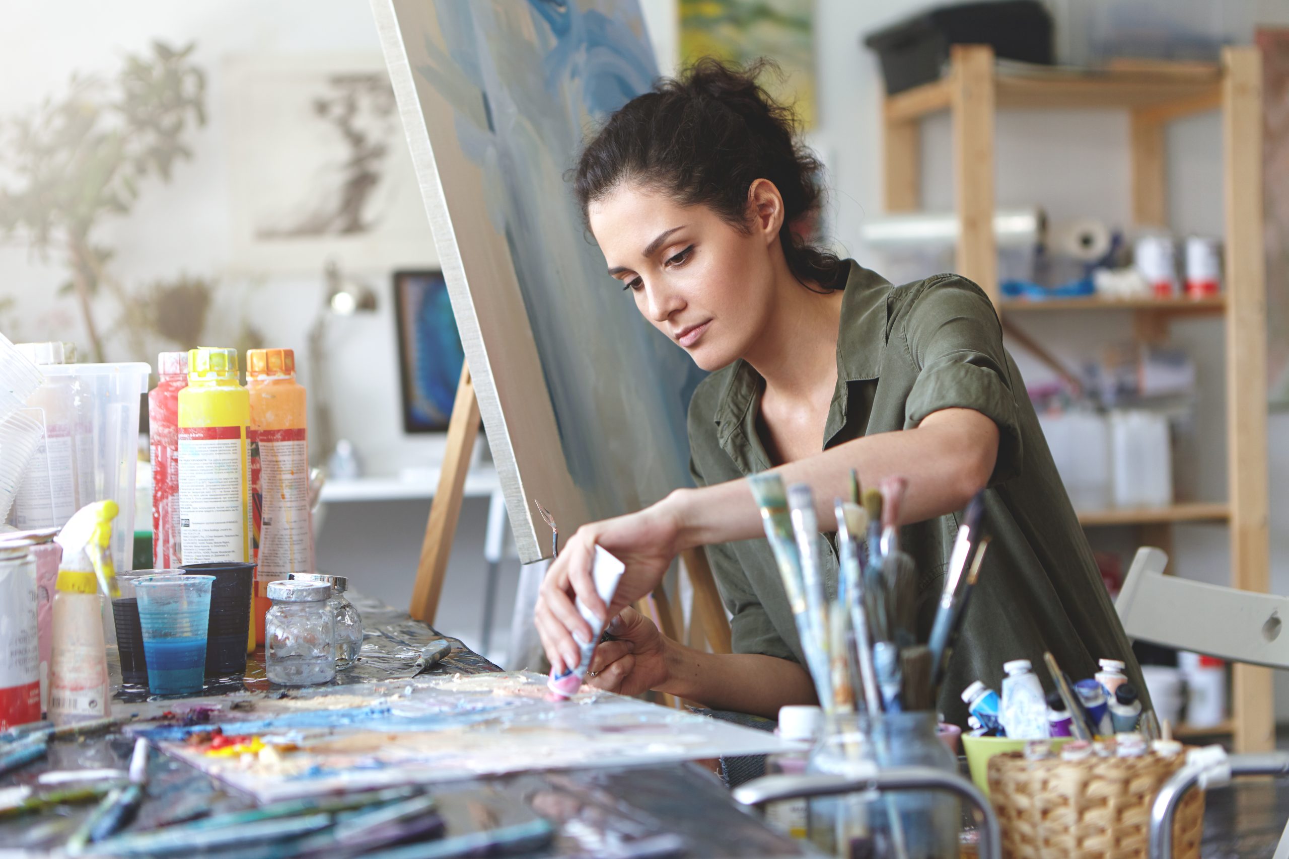A person painting on a canvas. The table has several paint boxes and tools. Painting is a self care tip for mental health and emotional health.