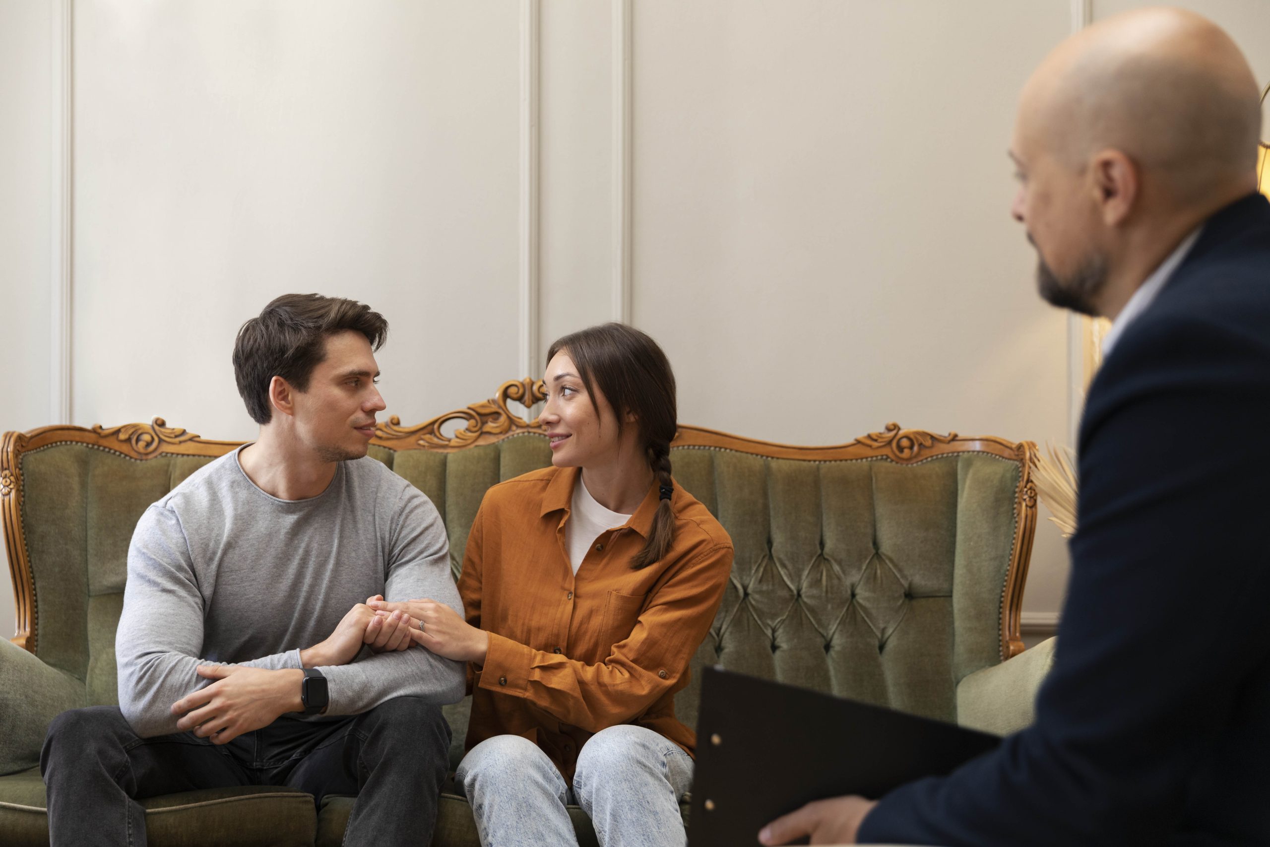 A couple is sitting opposite the Therapist to improve their relationship. The couple are holding hands and looking at each other lovingly.
