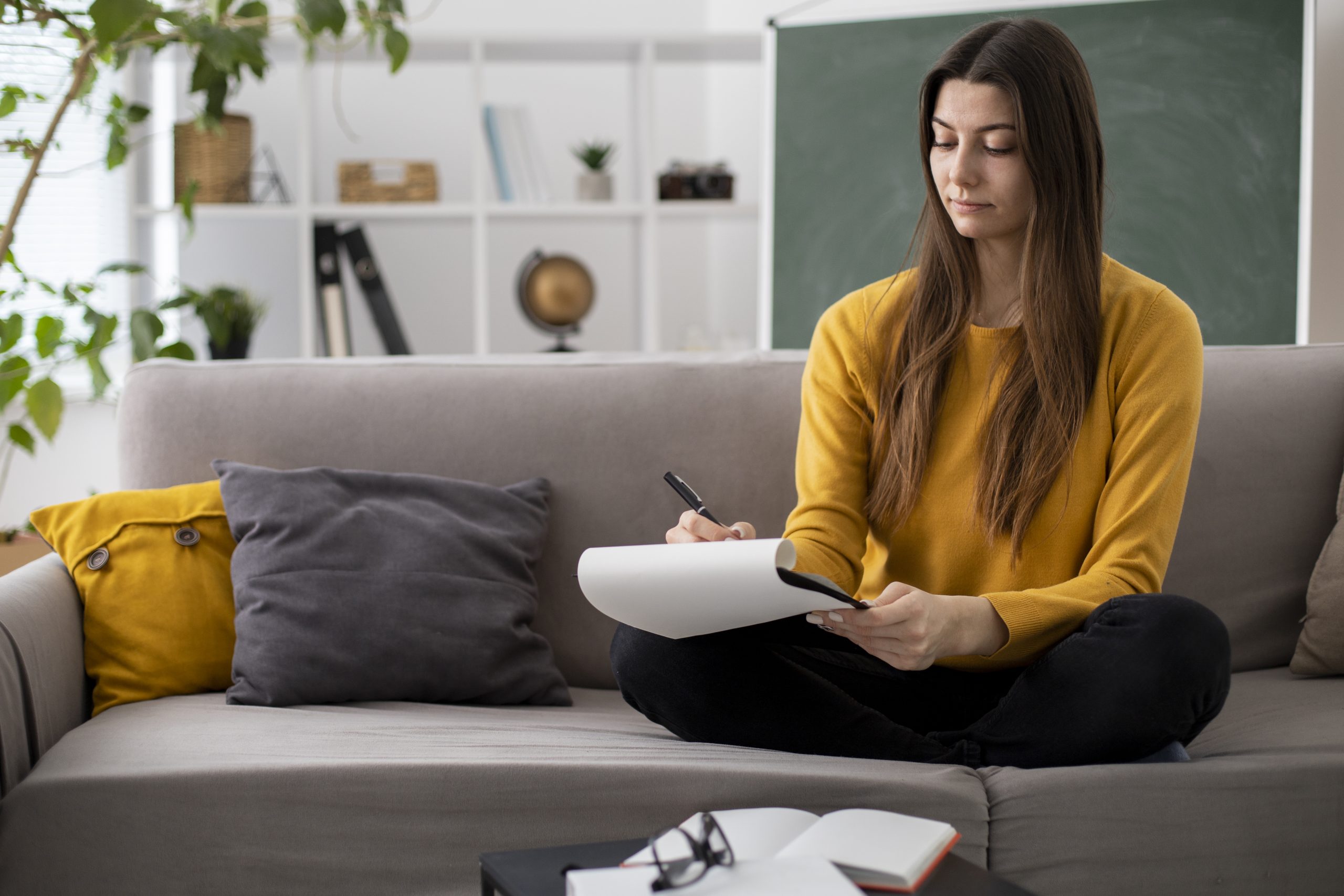 A person sitting on the couch with a pen and a notepad to take notes before the counselling session.