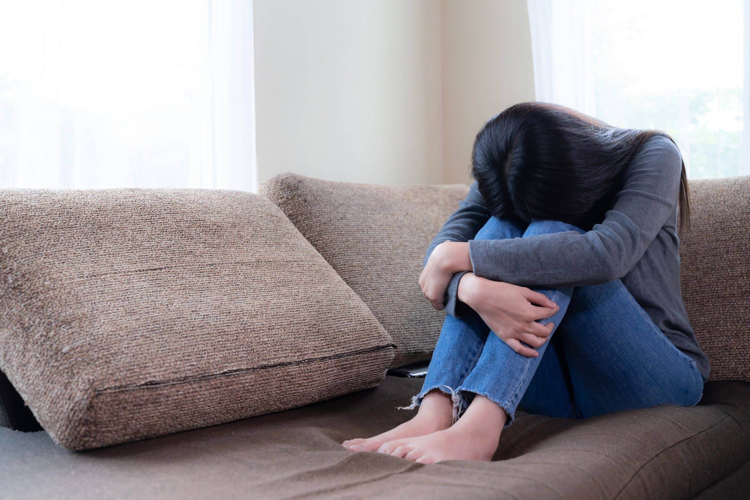 A distressed person sitting on the sofa with their head bent down, indicating suffering from a psychological disorder.